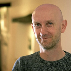 Portrait of a man with short hair and a beard, smiling and wearing a checked shirt.