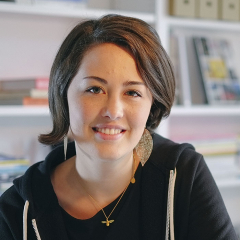 Portrait of a woman with long brown hair, wearing a black top, smiling in an office setting.