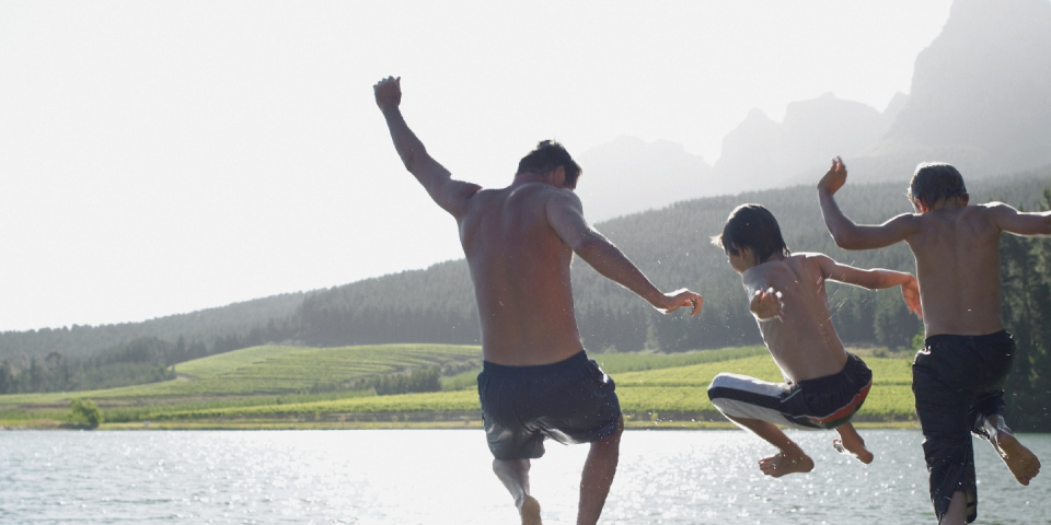 Adults and children jump into a lake on a sunny day