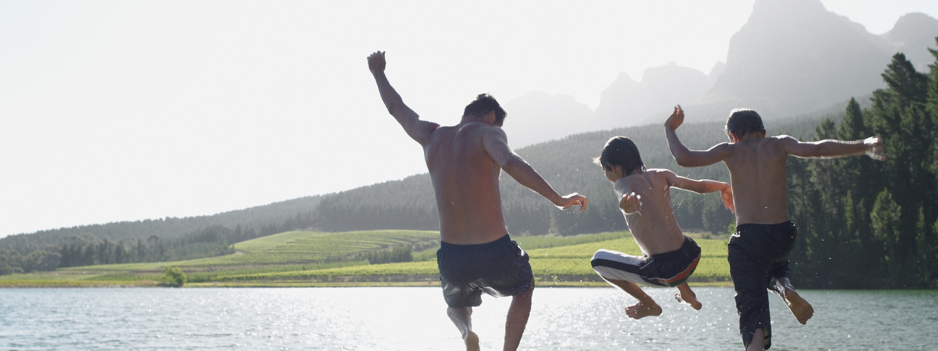 Adults and children jump into a lake on a sunny day