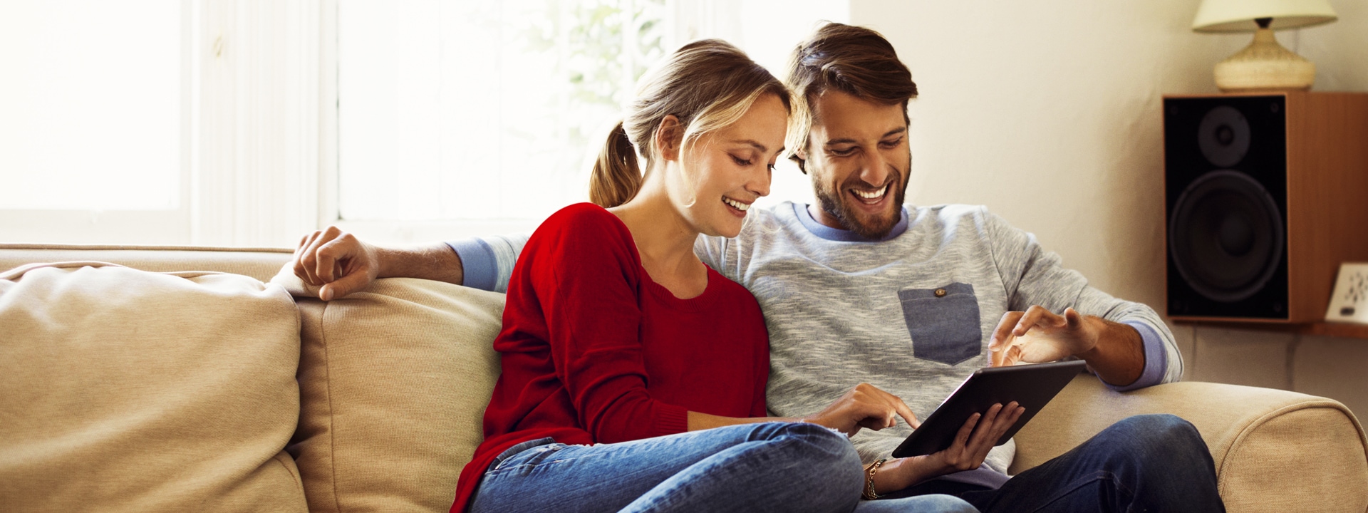 Couple sitting on a sofa at home, looking at a tablet device.