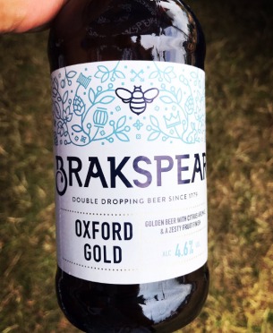 Hand holding a beer bottle with label. The label features a decorative floral and bee design at the top. Visible text includes: 