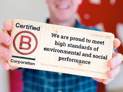 A photo of the author holding B Corp Certification plaque in mark-making*s reception